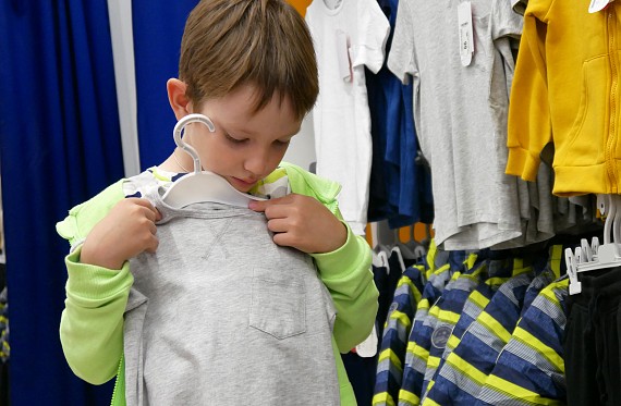 Young boy holding up a t-shirt in a charity shop.